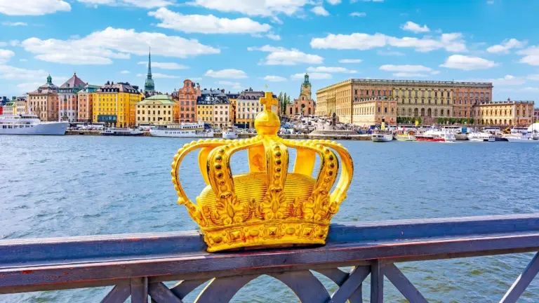 A Gold Crown On A Railing Over Water With Buildings In The Background