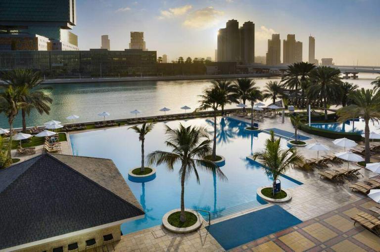 A Pool With Palm Trees And A City In The Background