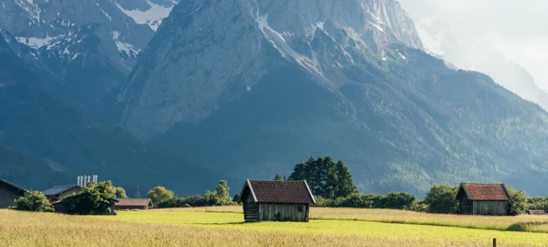 A Small Cabin In A Field With Mountains In The Background