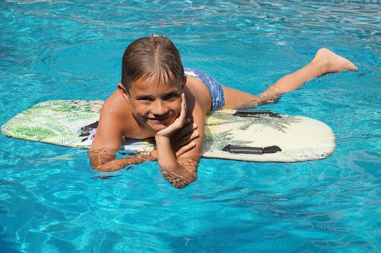 A Boy Lying On A Surfboard In A Pool