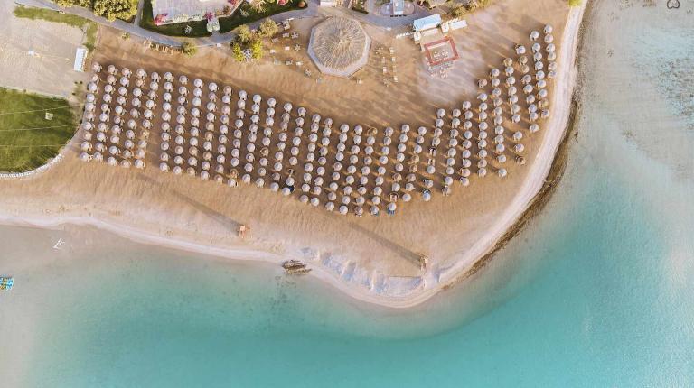 An Aerial View Of A Beach With Umbrellas And A Body Of Water